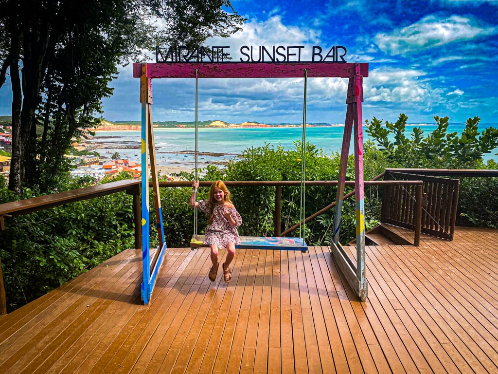 a child on a large swing overlooking the ocean at the mirante sunset bar.