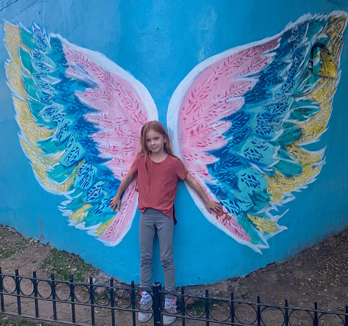 child with angel wing mural behind her