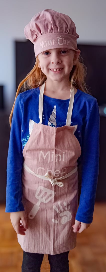 Kaia in a chefs hat and apron with the words "Mini Chef" on the front.