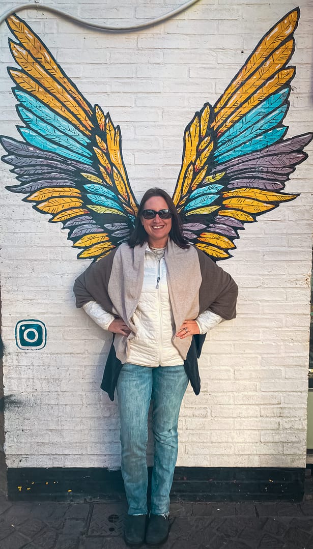 a women standing in front of a mural of angel wings