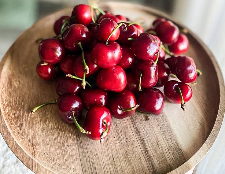 a wood board with fresh cherries on it.