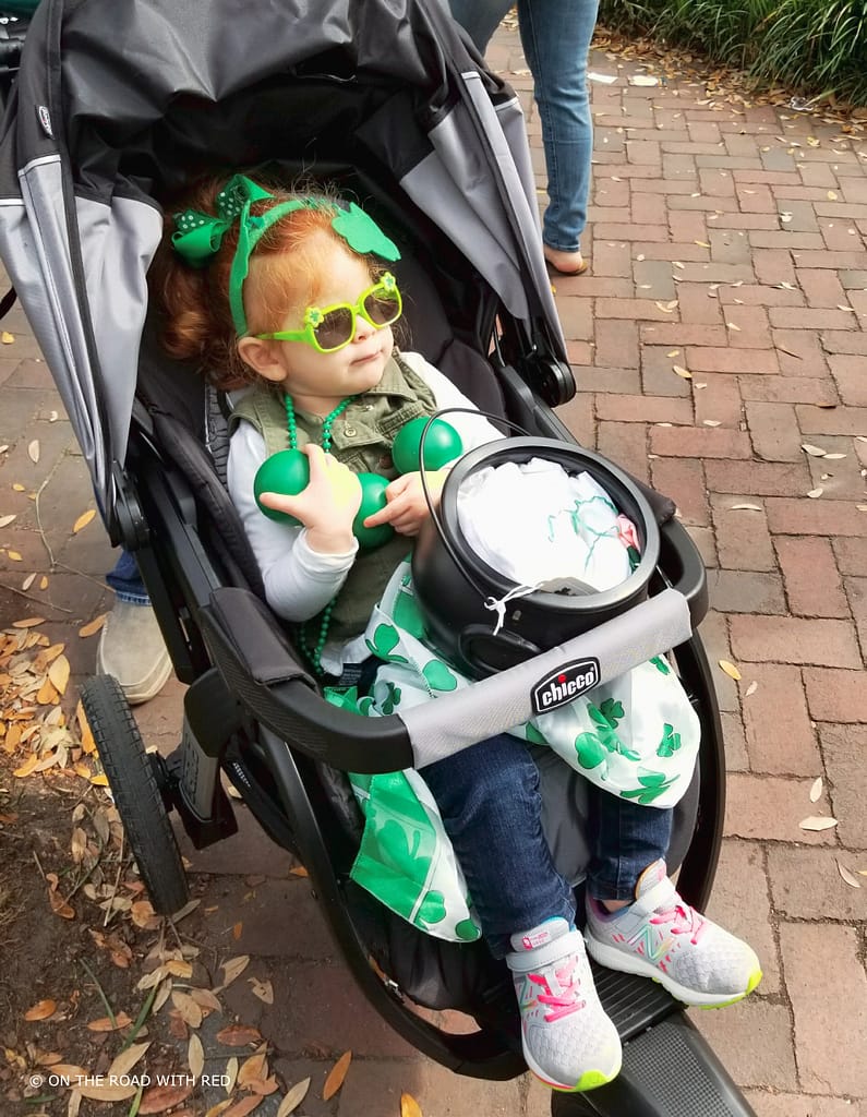 a toddler in a stroller with green clothing and toys