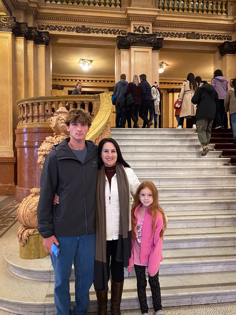 a mother and two children standing in front of a grand staircase.