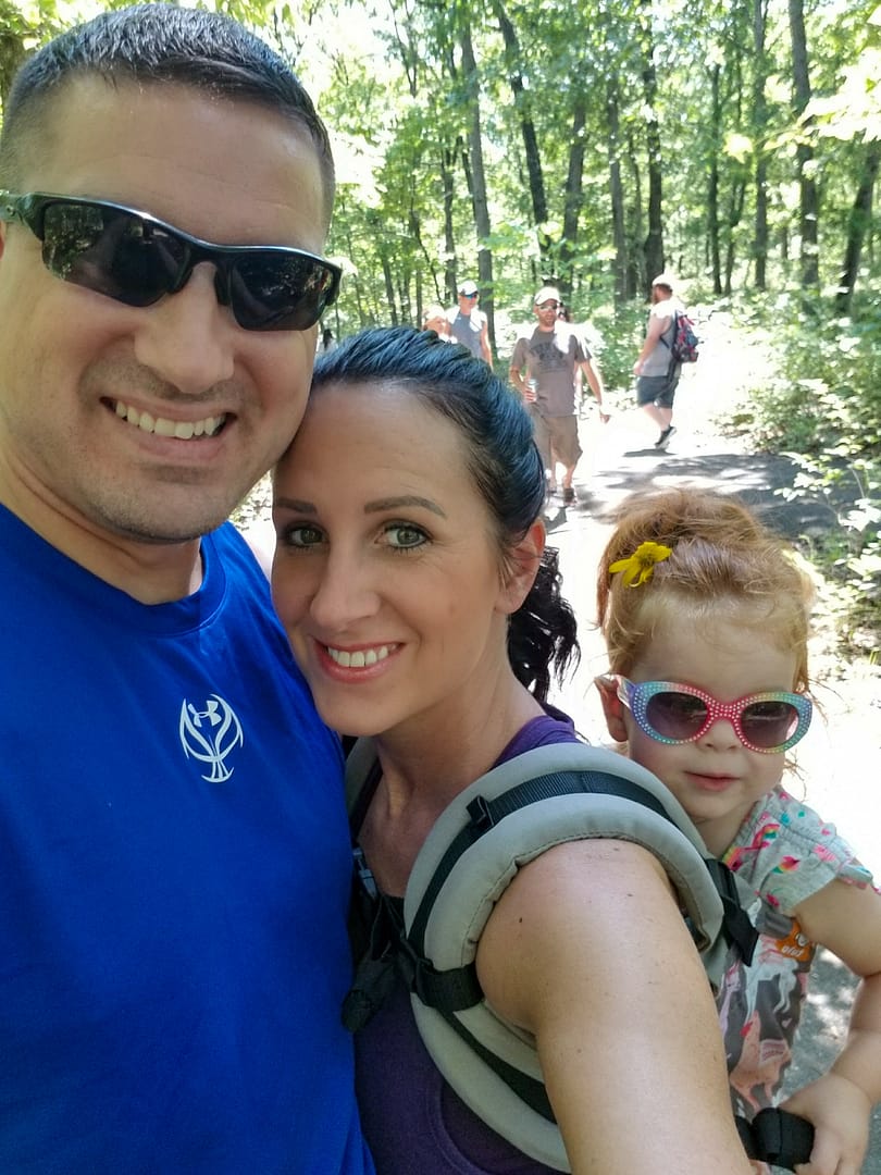 a man and woman with a toddler in a carrier in the forest.
