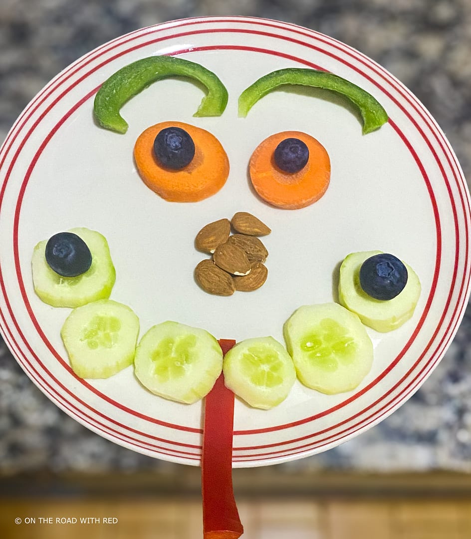 a plate with a face made out of veggies and almonds